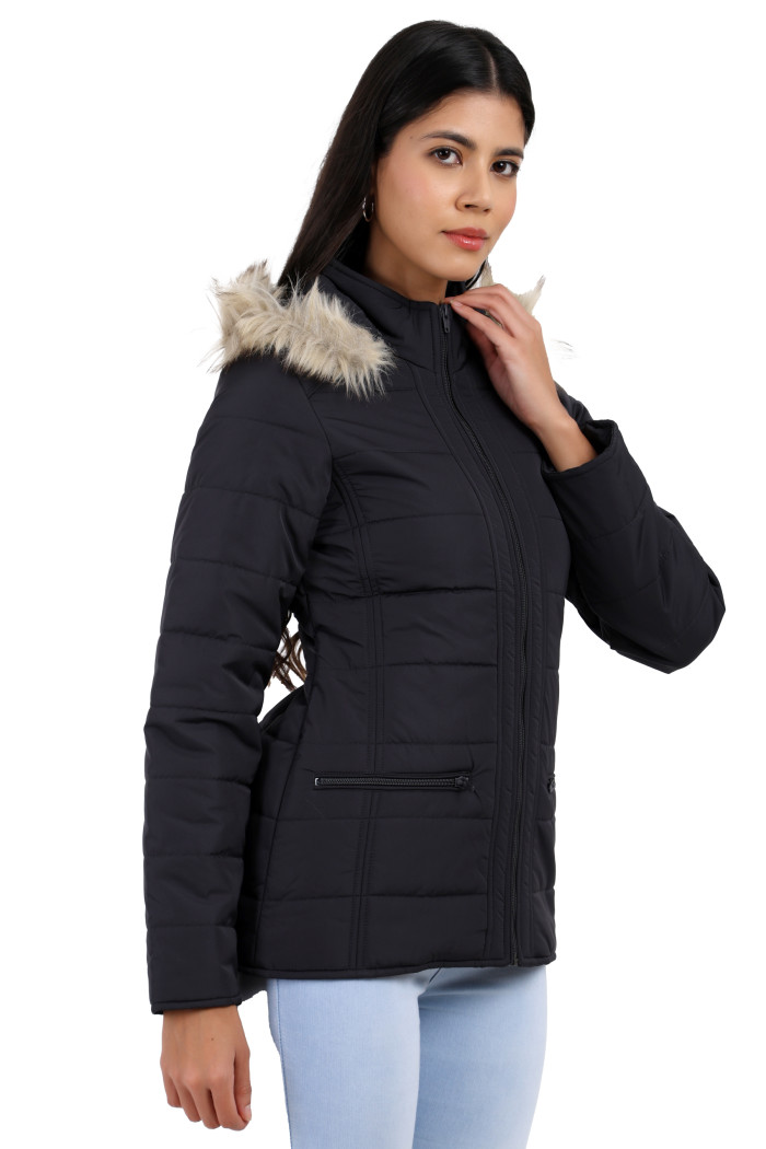 A woman in a standing side pose is wearing Trufit’s dark grey Matte Quilted Jacket with horizontal pockets, zip closure, a removable hood, and blue jeans with her left hand on the collar.